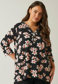 Tunic nera floreale con maniche 3/4, caratterizzata da fiori bianchi e rossi, scollatura a V e dettaglio con bottoni al collo. Tessuto morbido con una vestibilità comoda.