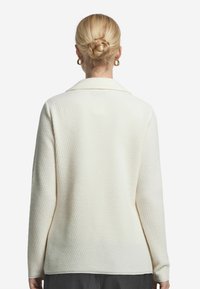 Cremiger, strukturierter Strickcardigan mit Kragen, langen Ärmeln und geradem Schnitt. Verfügt über ein dezentes Muster und eine lockere Passform.