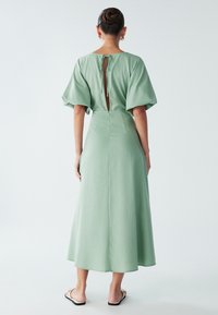 Ljusgrön klänning i midi-längd med nyckelhålsrygg, strukturerade korta ärmar och slät textur. Avslappnad passform med en flödande siluett.