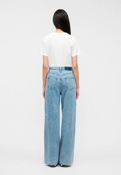 Λευκό μπλουζάκι σε συνδυασμό με ψηλόμεσα, ανοιχτόμπλε τζιν παντελόνια με φαρδιά μπατζάκια, πίσω τσέπες και γυρισμένα τελειώματα.