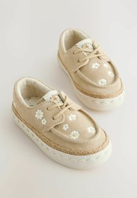 Chaussures en suède beige avec broderie de marguerites blanches, bout rond et semelle en caoutchouc blanc texturé avec des accents en corde le long du bord.