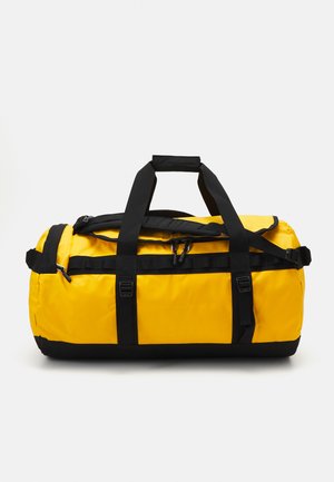 Yellow duffel bag with black accents, durable material, rounded shape, dual handles, and adjustable shoulder strap. Secure zipper closure.