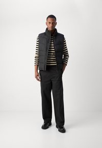 Black puffer vest over a black and cream striped long-sleeve shirt; paired with black wide-leg pants and black shoes. Smooth texture, minimal design.