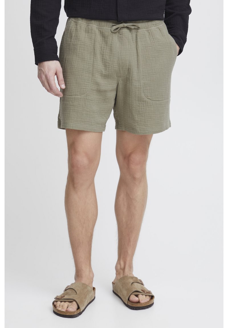 Olivgrüne Shorts aus strukturiertem Stoff mit elastischem Bund und Kordelzug. Mit zwei Taschen vorne und einem lockeren Schnitt.