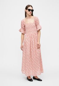 Γυναίκα που φοράει μαύρα γυαλιά ηλίου και μαύρα φλατ παπούτσια, με φόρεμα ροζ, με floral σχέδιο, τοπ με σφηκοφωλιά, φουσκωτά μανίκια και φούστα που ρέει.