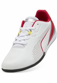 Scarpa sportiva bianca con accenti rossi, design perforato, lacci e suola nera. Presenta una tomaia texturizzata e un colletto imbottito.