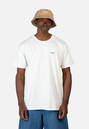 Weißes Baumwoll-T-Shirt mit Rundhalsausschnitt, das ein kleines schwarzes Logo auf der linken Brust trägt. Kombiniert mit lockeren blauen Denim-Shorts und einem beigen Bucket Hat.