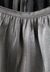 Šedá skládací tkanina s měkkou, lesklou texturou a prošívaným lemem, vykazující svislé linie a jemné odchylky ve stínování.