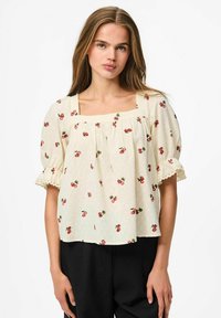 Blusa crema con maniche a puff corte, scollatura quadrata e stampa di ciliegie. Tessuto texture, dettagli in pizzo sui bordi delle maniche.
