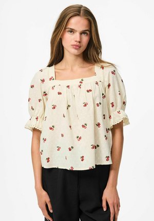 Blouse crème avec de courtes manches bouffantes, décolleté carré et imprimé cerise. Tissu texturé, détails en dentelle sur les bords des manches.