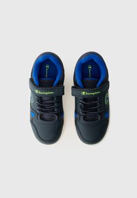 Zapatillas deportivas negras con acentos azules, detalles de malla, correa ajustable y diseño de cordones. Presenta detalle de logo y plantillas acolchadas.