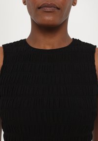 Rochie neagră cu textură plisată vertical, decolteu rotund și design fără mâneci. Țesătura pare ușoară și elastică.