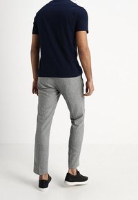 Een marineblauw shirt met korte mouwen gecombineerd met lichtgrijze, gestructureerde broeken en zwarte sneakers. De outfit heeft een ontspannen pasvorm en subtiele patronen.