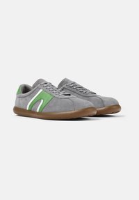 Sneaker in suede grigio con dettagli verdi e bianchi, caratterizzati da punta arrotondata e suola in gomma marrone. I lacci sono grigi e la fodera è in morbido tessuto grigio.