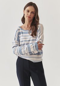 Maglione a maniche lunghe a righe blu e bianche con vestibilità comoda, scollatura ampia e texture morbida, abbinato a pantaloni scuri.