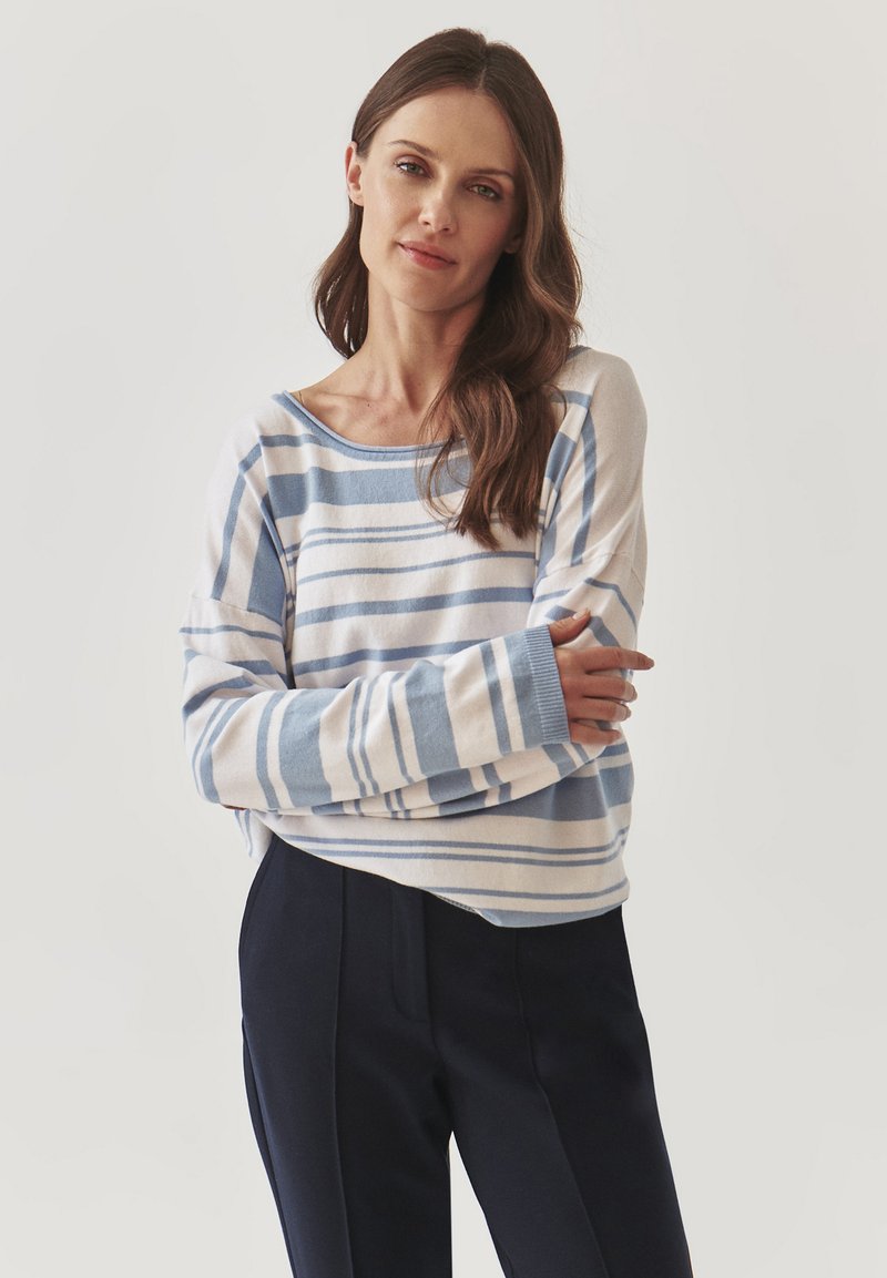 Maglione a maniche lunghe a righe blu e bianche con vestibilità comoda, scollatura ampia e texture morbida, abbinato a pantaloni scuri.