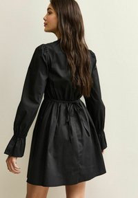Czarna sukienka do kolan z bufkami, paskiem ściągającym w talii i rozszerzanymi mankietami, wykonana z gładkiego materiału. Charakteryzuje się prostym wzornictwem.