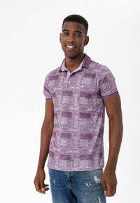 Kravefarvet polo skjorte med krave, der har et struktureret mønster i varierende nuancer; parret med slidte blå jeans.
