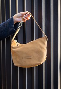 Borsa a tracolla in suede color tan con forma curvata, dotata di un clasp in metallo e del logo "SHABBIES" in rilievo. La tracolla è regolabile e testurizzata.