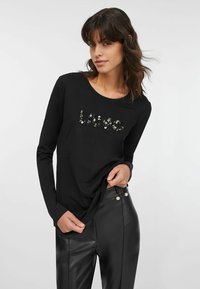 Camicia nera a maniche lunghe con la scritta "Love" in paillettes. Tessuto liscio, scollo arrotondato, abbinata a pantaloni neri in pelle a vita alta.