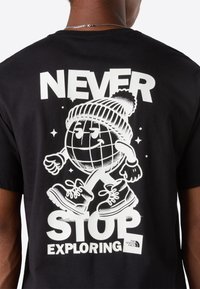 Back of black t-shirt with white graphic of globe character wearing a beanie and boots, text "Never Stop Exploring," The North Face logo.