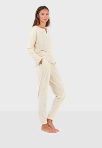 Ensemble de vêtements de détente de couleur crème comprenant un haut à manches longues avec col à revers et un pantalon à cordon avec poches, orné de petits accents.