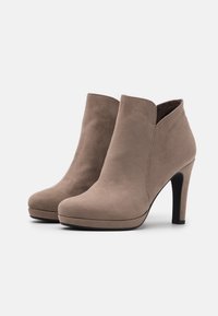 Botines de ante beige con tacón alto, punta redonda y un diseño recortado en el tobillo. Textura suave y detalle de costura sutil.