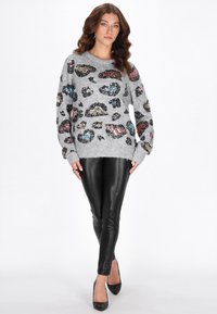 Pulover gri cu imprimeu de leopard din paiete multicolore, decolteu rotund, croială lejeră, combinat cu colanți negri din piele și tocuri negre.