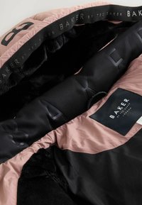 Interno di giacca rosa e nera che mostra foderatura in pelliccia nera e etichette del marchio "Baker by Ted Baker London" sul colletto e sul corpo.
