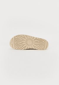 Sko såle med en teksturert, beige gummioverflate som har et solstrålemønster og riller for grep. Glatt kant rundt omkretsen.