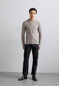 Gai pelēks tekstūrēts adīts džemperis ar dimanta rakstu, kombinēts ar tumšajiem taisnajiem džinsiem un spīdīgām melnām kurpēm. Vienkāršs dizains, pieguļošs siluets.