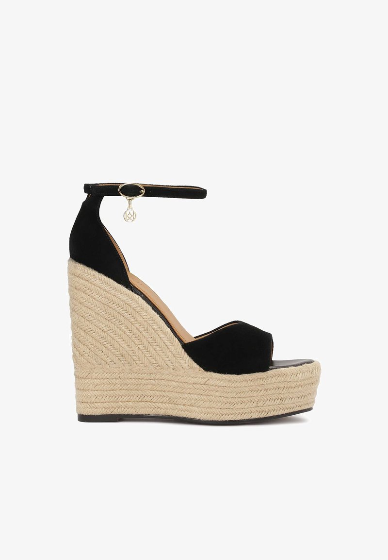 Sandale compensée en daim noir avec une plateforme en jute tissée, une bride de cheville avec un charme en ton doré et un design à bout ouvert.
