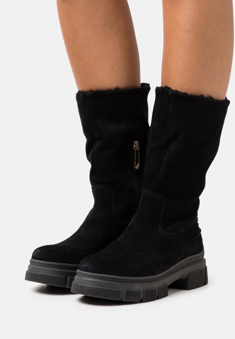 Bottes noires en suède montant jusqu'aux genoux avec une texture douce, équipées d'une fermeture éclair latérale et de semelles épaisses en caoutchouc pour la stabilité.