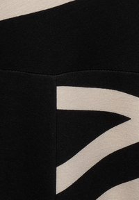 Mustavalkoinen kangas, jossa on voimakas, abstrakti sahalaitakuviot. Materiaali on sileä ja tekstuuri, jossa on hyvin erottuvat kontrastivärit.