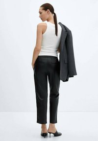 Černé kožené kalhoty s volným střihem, kombinované s upnutým bílým tílkem. Tmavě šedý blazer přehozený přes rameno, stylové podpatky.