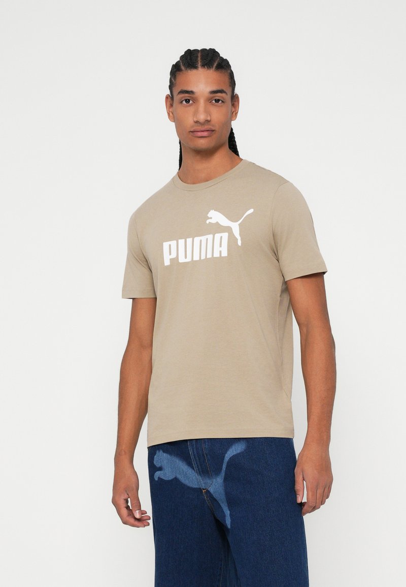 Bež pamukasta majica s okruglim izrezom, koja na prednjoj strani ističe veliki bijeli "PUMA" logo i grafiku skakutajuće pumice.