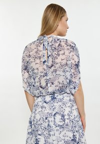 Rochie ușoară, transparentă, de culoare albă, cu model floral albastru. Prezintă o închidere cu legătură la spate și mâneci scurte, cu un design liber și fluid.