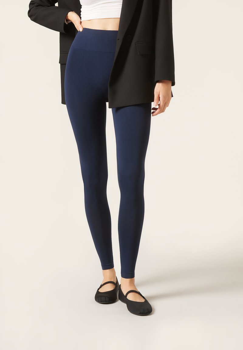 Mørkeblå leggings lavet af strækbart stof, med høj talje, parret med sorte flade sko og en oversized sort blazer.