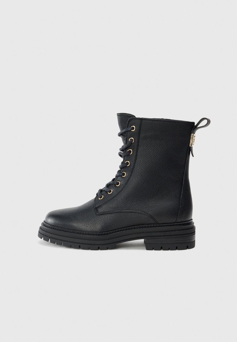 Botte de combat en cuir noir à lacets avec œillets dorés, semelle épaisse à crampons et languette à l'arrière.
