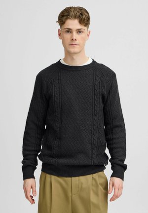 Black knitted sweater with a textured diamond pattern, ribbed cuffs, and hem; crew neckline; worn over a white T-shirt.