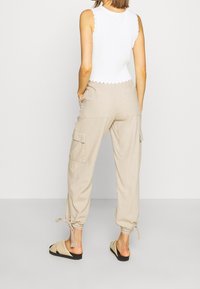 Beige cargo pants with elastic cuffs, two side pockets, and drawstring detail. Paired with a white sleeveless top featuring a scalloped hem.
