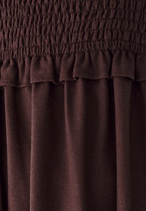 Brūns auduma tops ar savelkošu smokošanas detaļu, ruffled apakšmalu un mīkstu tekstūru, radot plūstošu dizainu ar smalkām krokām.