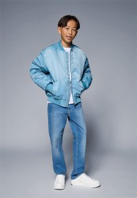 Lyseblå satin bomberjakke med ribbestrikkede mansjetter og hem. Brukt over en hvit t-skjorte, kombinert med blå jeans og hvite sneakers.