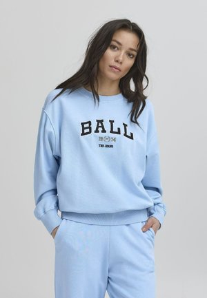 Šviesiai mėlynas sportinis treniruoklis su laisvu kirpimu, susiraukšlėjusiais rankogaliais ir juodu grafiniu tekstu "BALL 1974 THE JEANS" per priekinę dalį. Kišenės detalė ant kelnių.
