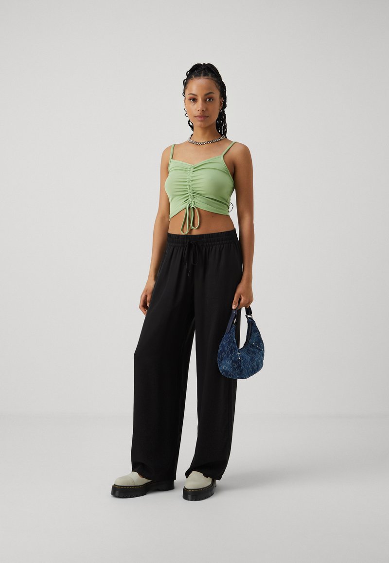Zelený rebrovaný crop top s detailom na šnúrku, čierne široké nohavice a modrá štruktúrovaná kabelka, doplnené bielosolmi čiernych topánok.