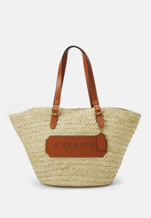 Vävd halm tote-väska med bruna läderremmar och varumärke. Innehåller en rektangulär läderlapp med präglad text och en bagagetagg.