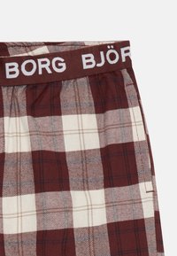 Boxers em xadrez vermelho e branco para homens com um cós elástico castanho com "BJÖRG" em letras brancas. Material de algodão, textura suave.