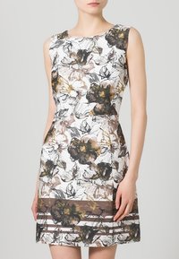 Vestido de estampado floral con diseño sin mangas. Presenta un fondo blanco, patrones florales multicolores en marrón y negro, y una silueta estructurada.