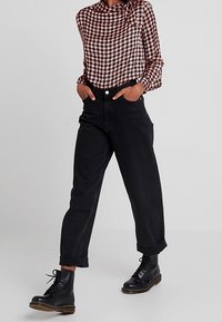 Svarta högmidjade jeans med uppvikta fållar, tillsammans med en blus i röd och svart houndstooth-mönster. Svarta snörstövlar fulländar outfiten.