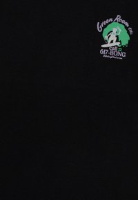 Surfista sosteniendo dos pinceles montando una ola verde con el texto "Green Room Co." y "llama al 617-BONG Billabong Surf service" sobre una tela negra.